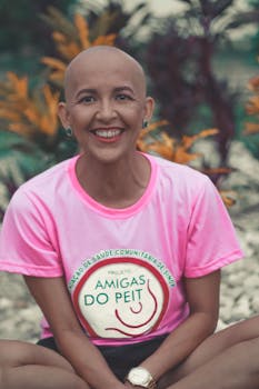 Joyful bald woman sitting outdoors in a pink cancer awareness t-shirt, promoting positivity.